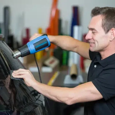 Technician applying 3M car window tint film with heat gun at Samrat Auto 3M-authorized car care center in Dubai